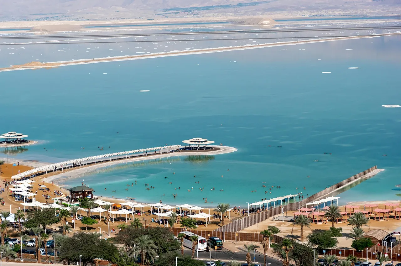 The Dead Sea shoreline and resort area viewed from above, showing the turquoise water and arid Judean landscape