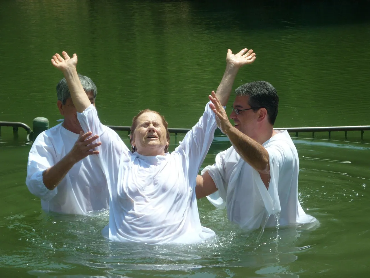 Pilgrims in white robes wading into the Jordan River at Yardenit baptismal site near the Sea of Galilee