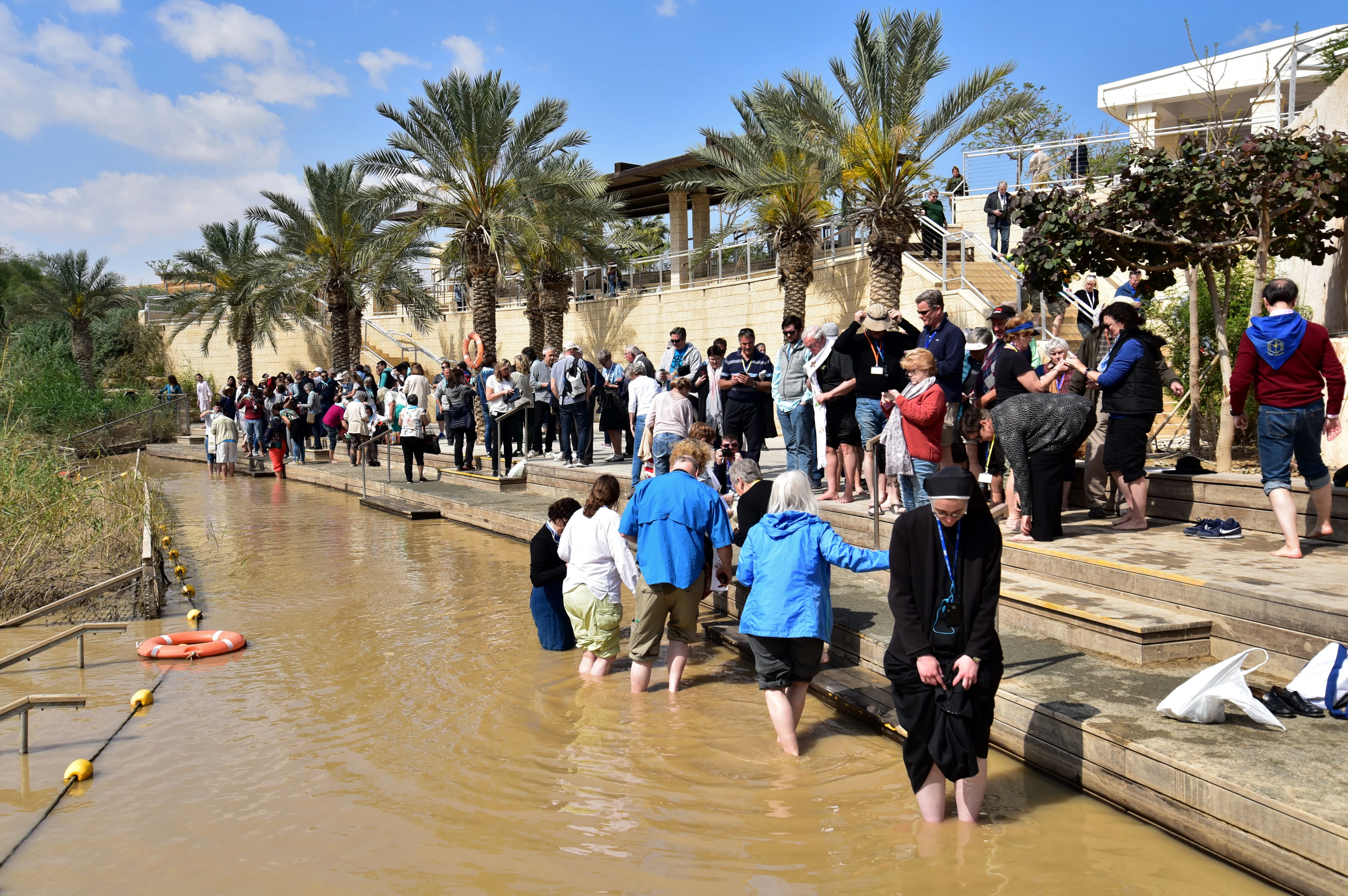 Christian pilgrim group dressed in white baptismal robes gathered at the Jordan River for a group baptism service